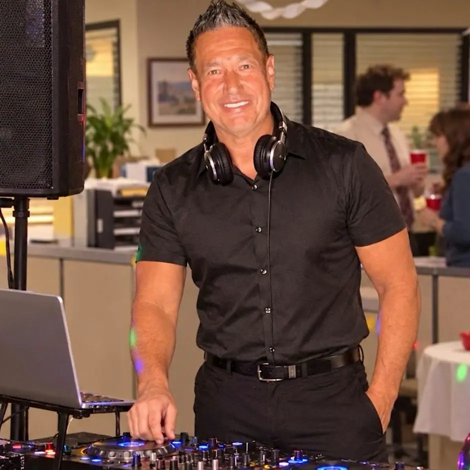 Celebrity DJ Baltazar smiling at his mixing console with headphones around his neck