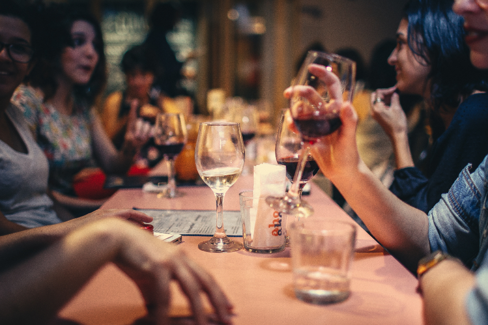 Friends laughing and raising glasses around a table at a lively bar